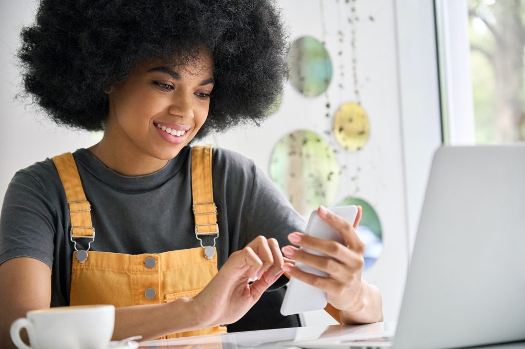 Afro American young woman in cafe holding phone with laptop shopping online.