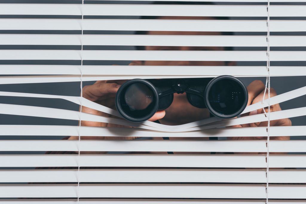 suspicious young man with binoculars spying through blinds