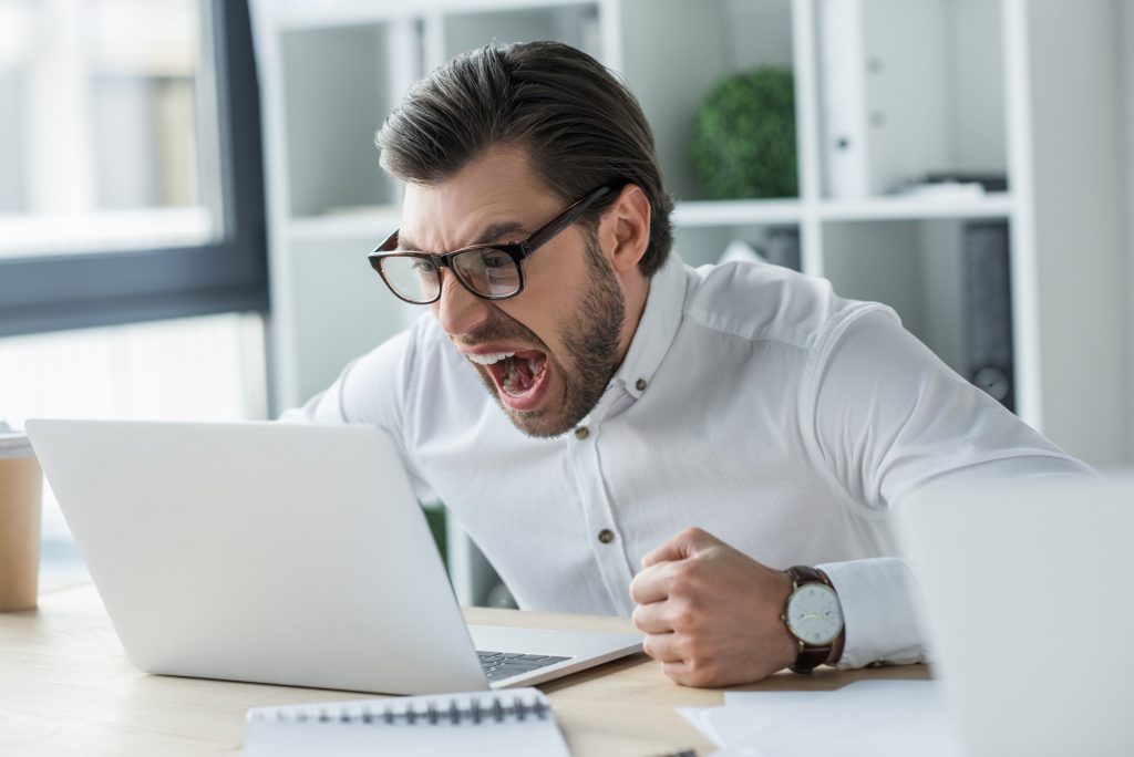 mad young businessman shouting at laptop in office