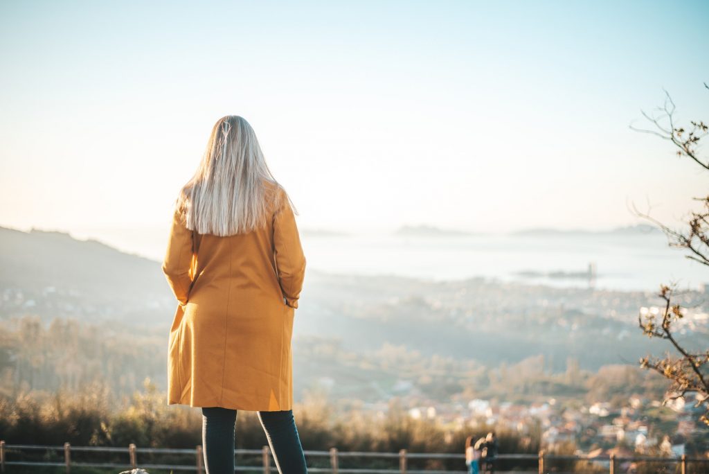 Woman on a yellow coat sitting on a bench contemplating the landscape